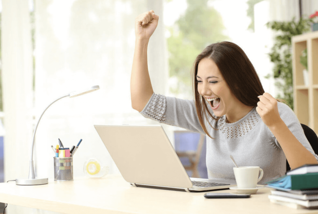 Woman smiling and cheering while looking at laptop screen