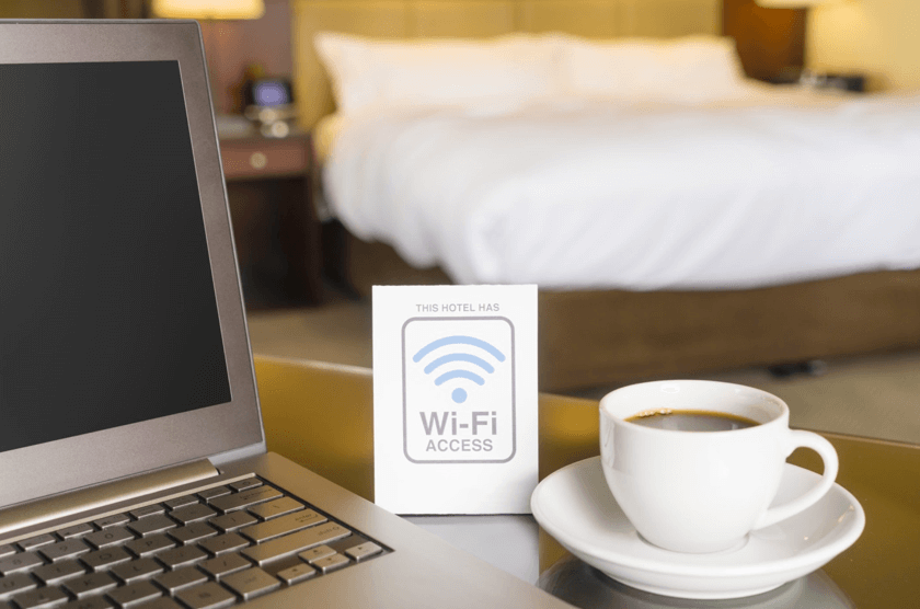 cup of coffee on saucer with laptop and wifi access notice on a table inside a hotel room