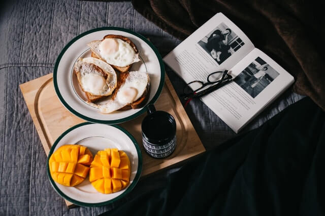breakfast plate and coffee on a wooden bed board with a book and reading glasses to the side
