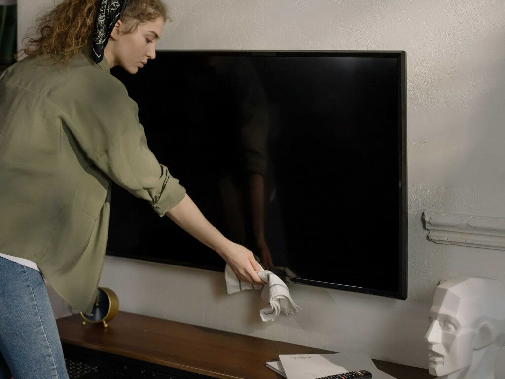 young woman dusting a flatscreen tv