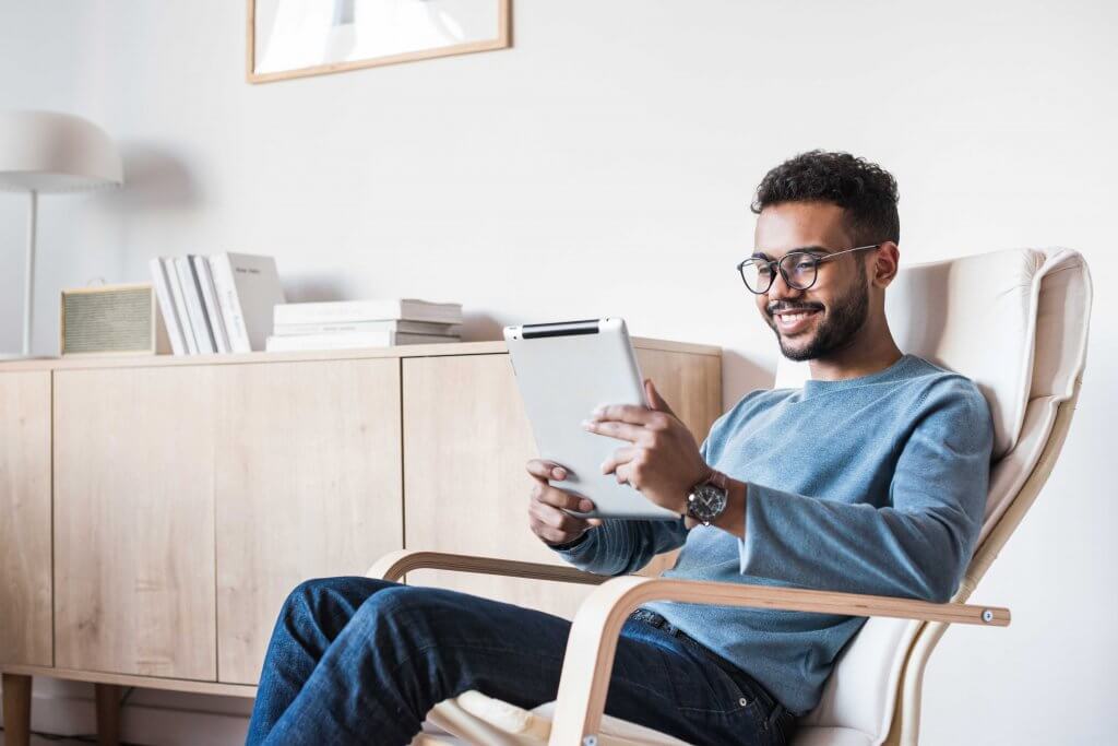 man smiling at tablet while sitting in a desk chair