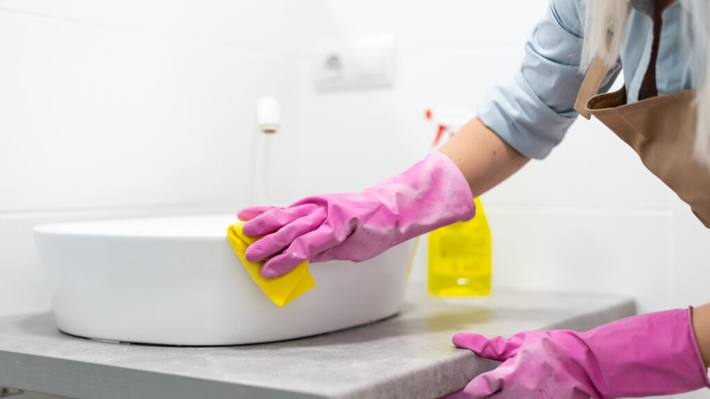 airbnb cleaner scrubbing down a bathroom sink while wearing gloves