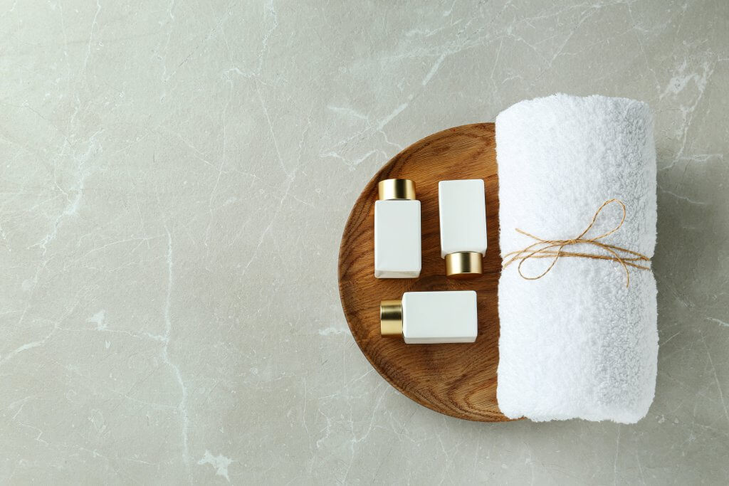 a wooden plate topped with three white soap bars and a rolled towel. 