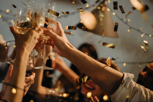 group of hands holding wine glasses while gold confetti floats around them