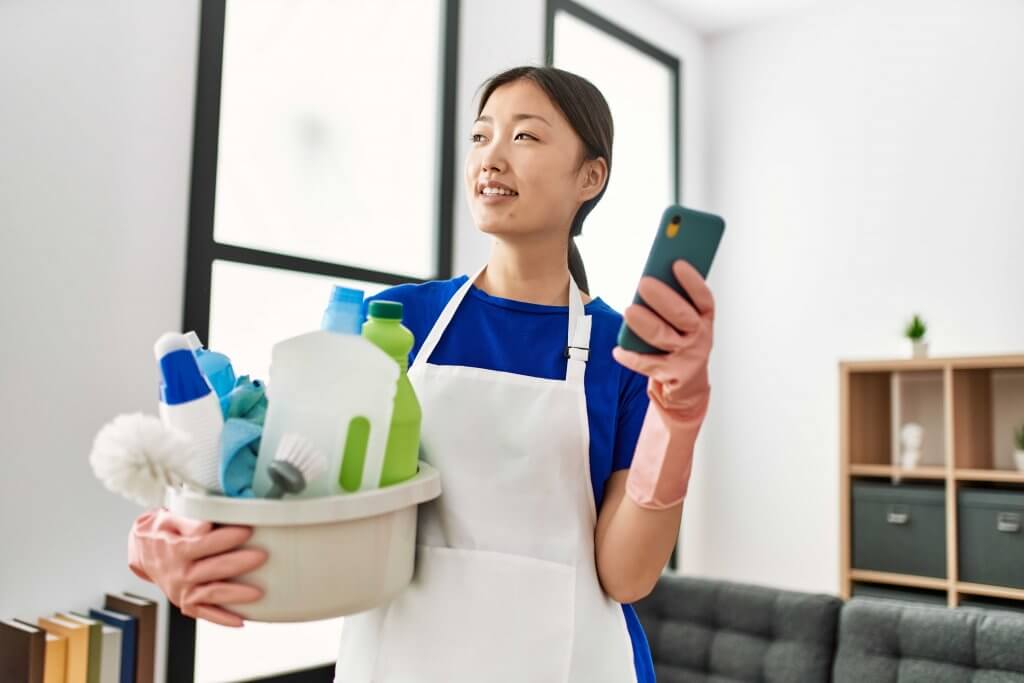 Cleaner on phone and holding caddy of cleaning supplies