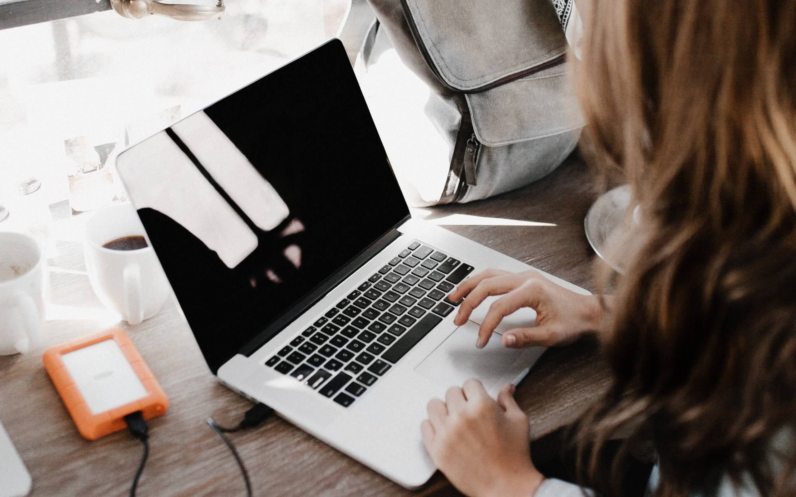 Woman with brown hair typing on a laptop while charging phone. 