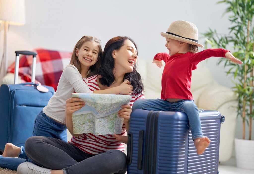 mom and two young daughters smiling while looking at a map in their living room near suit cases