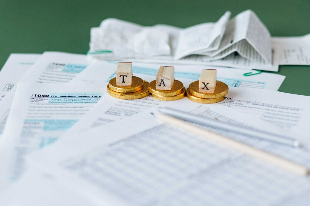 Tax paperwork in a pile with gold coins, receipts, and wooden letters spelling "tax"