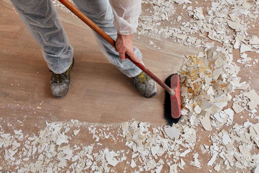 male sweeping broken dry plaster from wooden floors