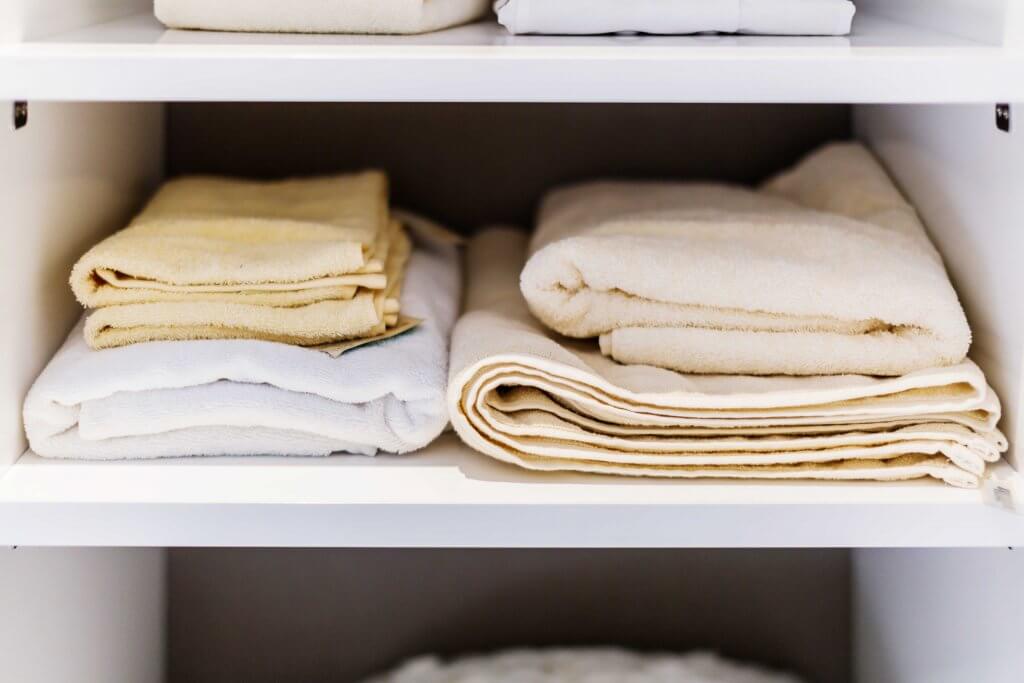 yellow and white towels folded and stacked on white shelves of a closet space