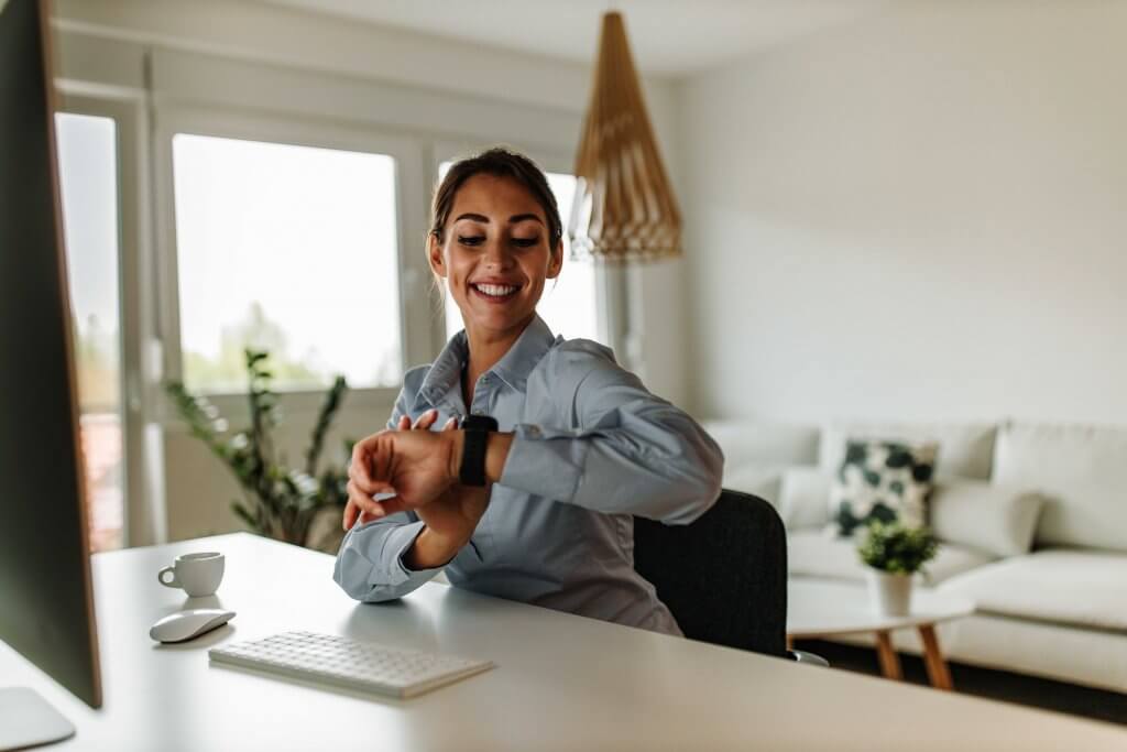 woman smiling at a desk while looking at her wrist watch