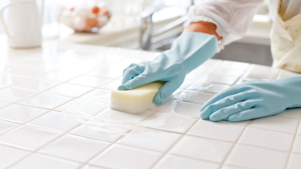 Gloved hands using a sponge to clean kitchen countertops