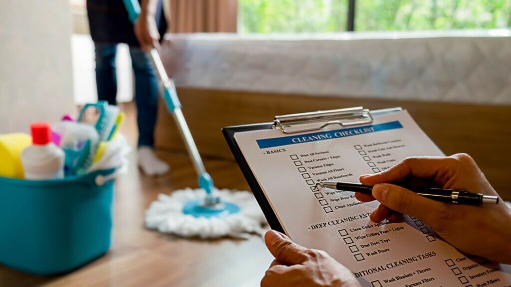 Airbnb cleaning tasks being marked done on a checklist while a cleaner mops in the background. 