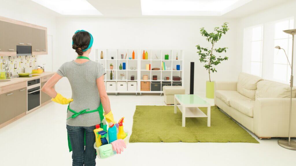 Airbnb cleaner standing in a clean room with a cleaning caddy in right hand. 