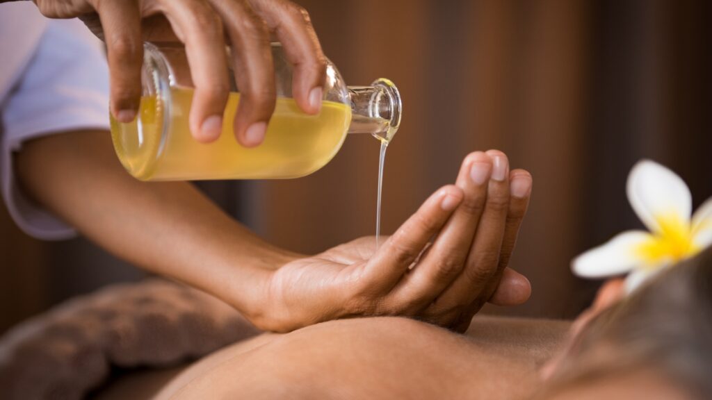 massage oil being poured in palm of hand over a woman's bare back