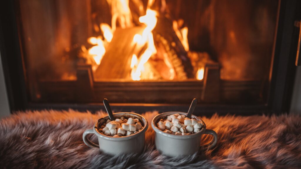 two cups of hot chocolate and marshmallows set in front of a fireplace in a winter airbnb  