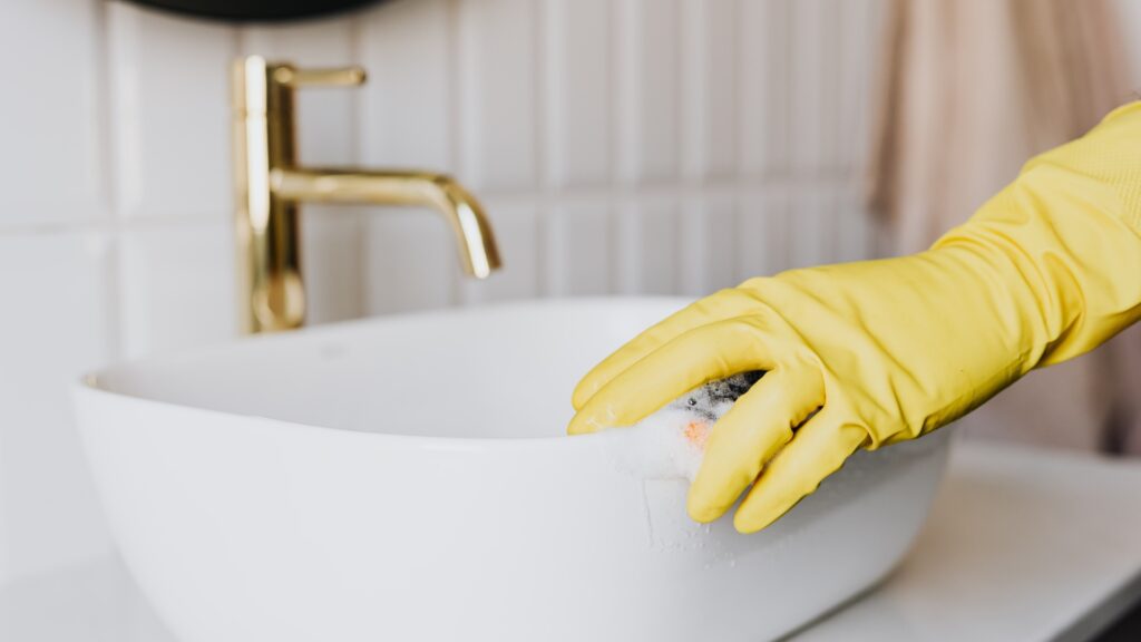 gloved hand washing rim of bathroom sink