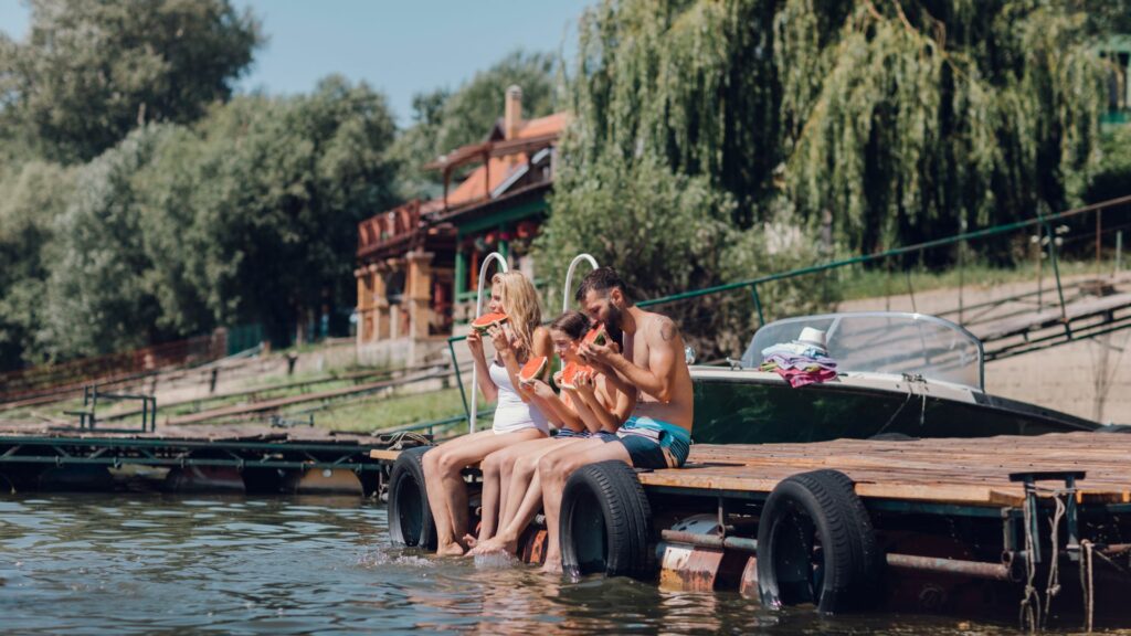 Family sitting on a lake doc eating watermelon during the summer at an airbnb
