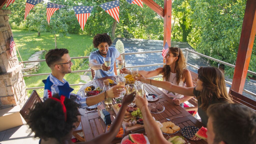 friends celebrating the 4th of july outside at a dinner table cheering