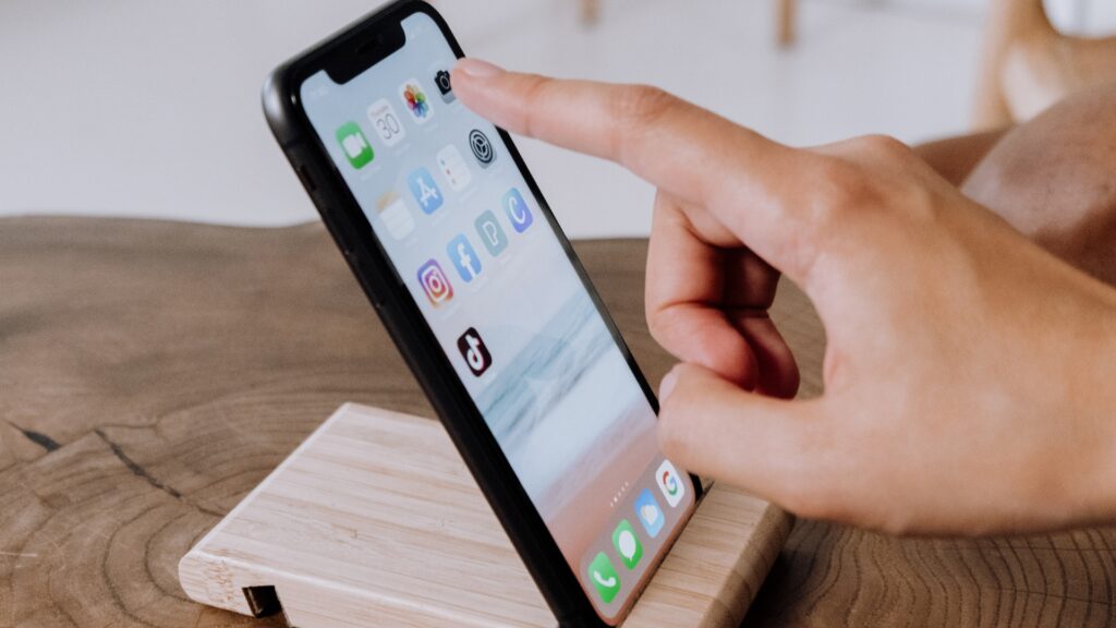 Iphone on a phone stand with a finger tapping the camera icon on the screen