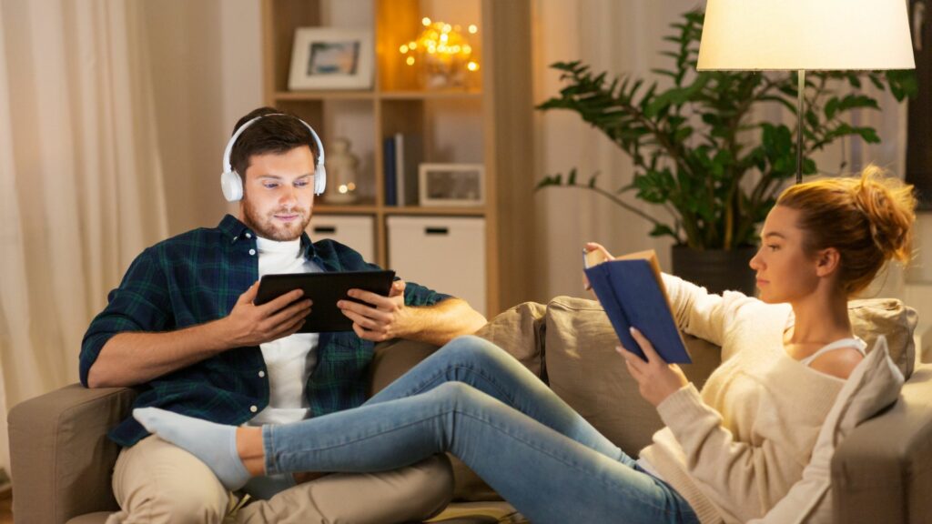 airbnb guest sitting on the couch while one is reading and the other is on a tablet 